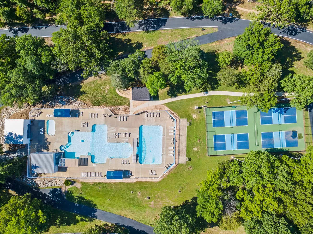 This image showcases a vibrant outdoor scene featuring a swimming pool surrounded by lush greenery and adjacent tennis courts. Poolside loungers invite relaxation, while the courts in the background hint at active recreation. The setting is bright and lively, emphasizing both relaxation and activity.