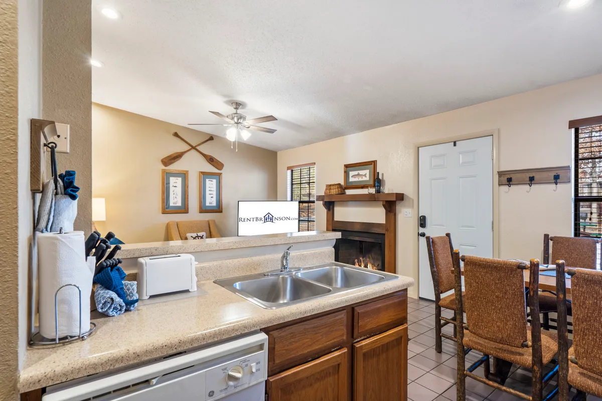 An open-plan view that seamlessly connects the kitchen, dining area, and living space. The image features a dining table, kitchen counter with modern appliances, a fireplace, and decorative paddles, offering a sense of flow and togetherness.