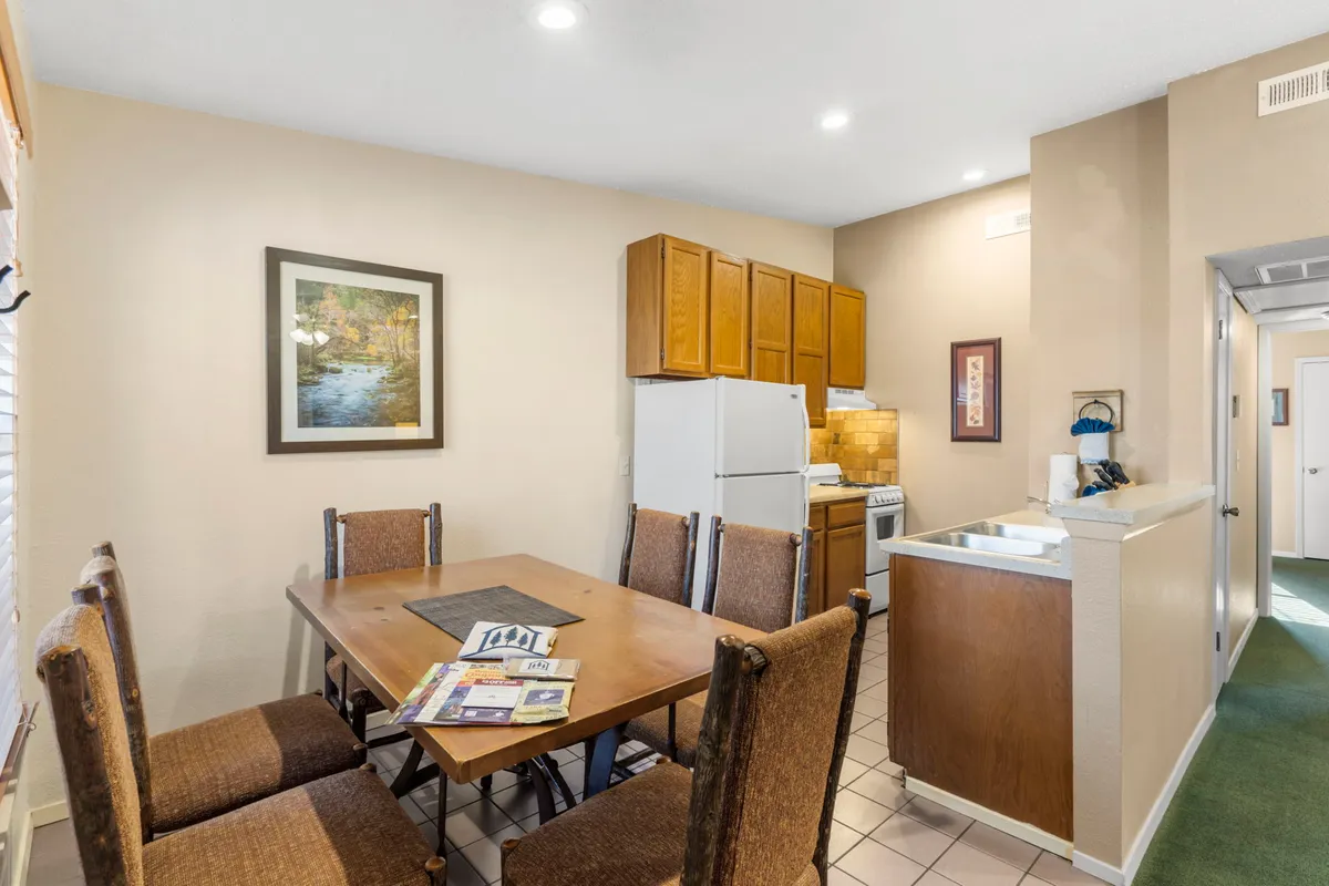 A cozy dining area with a wooden table and chairs adjacent to a bright kitchen space, accented by framed wall art. The setup is ideal for family meals, celebrations, or casual gatherings, and is filled with warmth and charm.