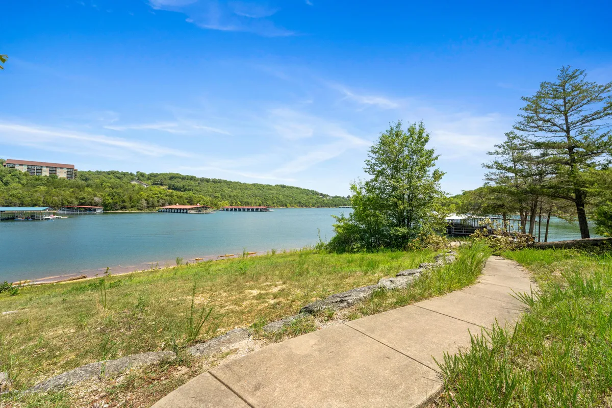 A serene view of a calm lake framed by lush greenery, with a gentle pathway leading down to the water’s edge. The open space is ideal for pet-friendly exploration and taking in the natural beauty together.