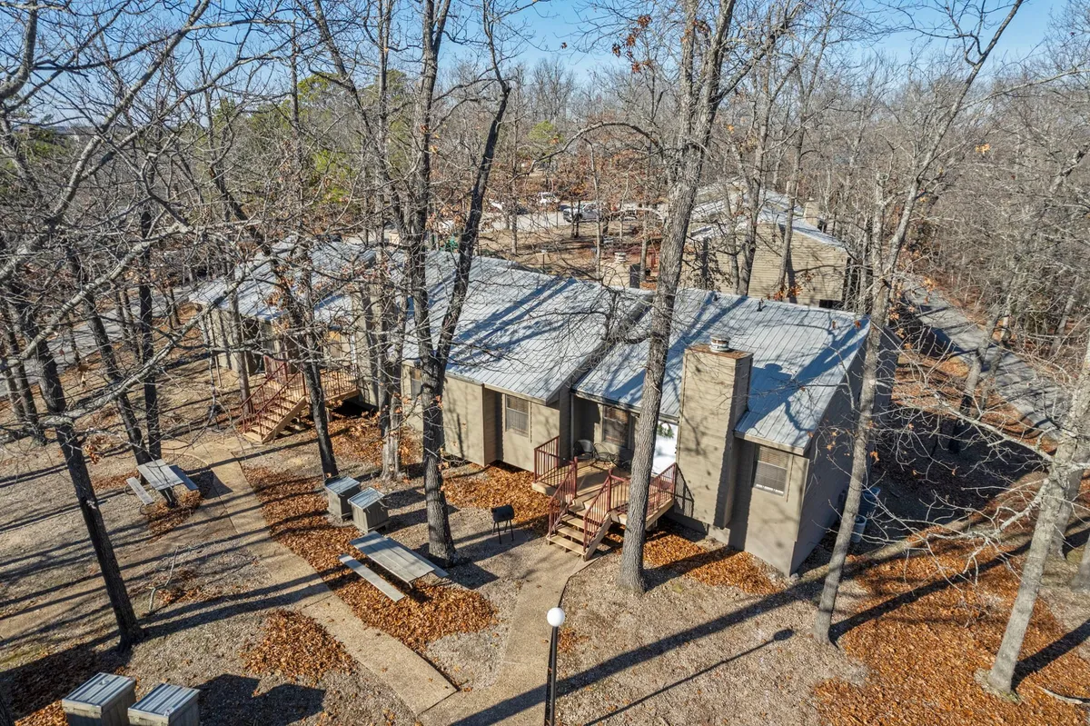 An exterior view featuring cabins set amongst trees with picnic tables and a winding pathway. The inviting landscape suggests spots for sunset picnics, nature walks, or relaxed moments together, ideal for couples seeking both adventure and tranquility.
