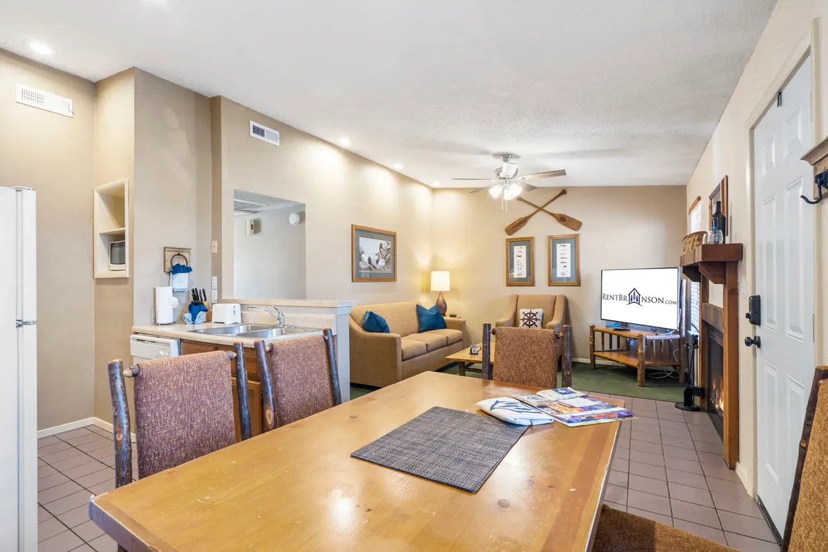 The image showcases a warm, inviting living and dining area featuring a cozy sofa, crackling fireplace, a dining table set for meals, and a television—creating the perfect space for family gatherings, movie nights, and relaxation after a day at Table Rock Lake.