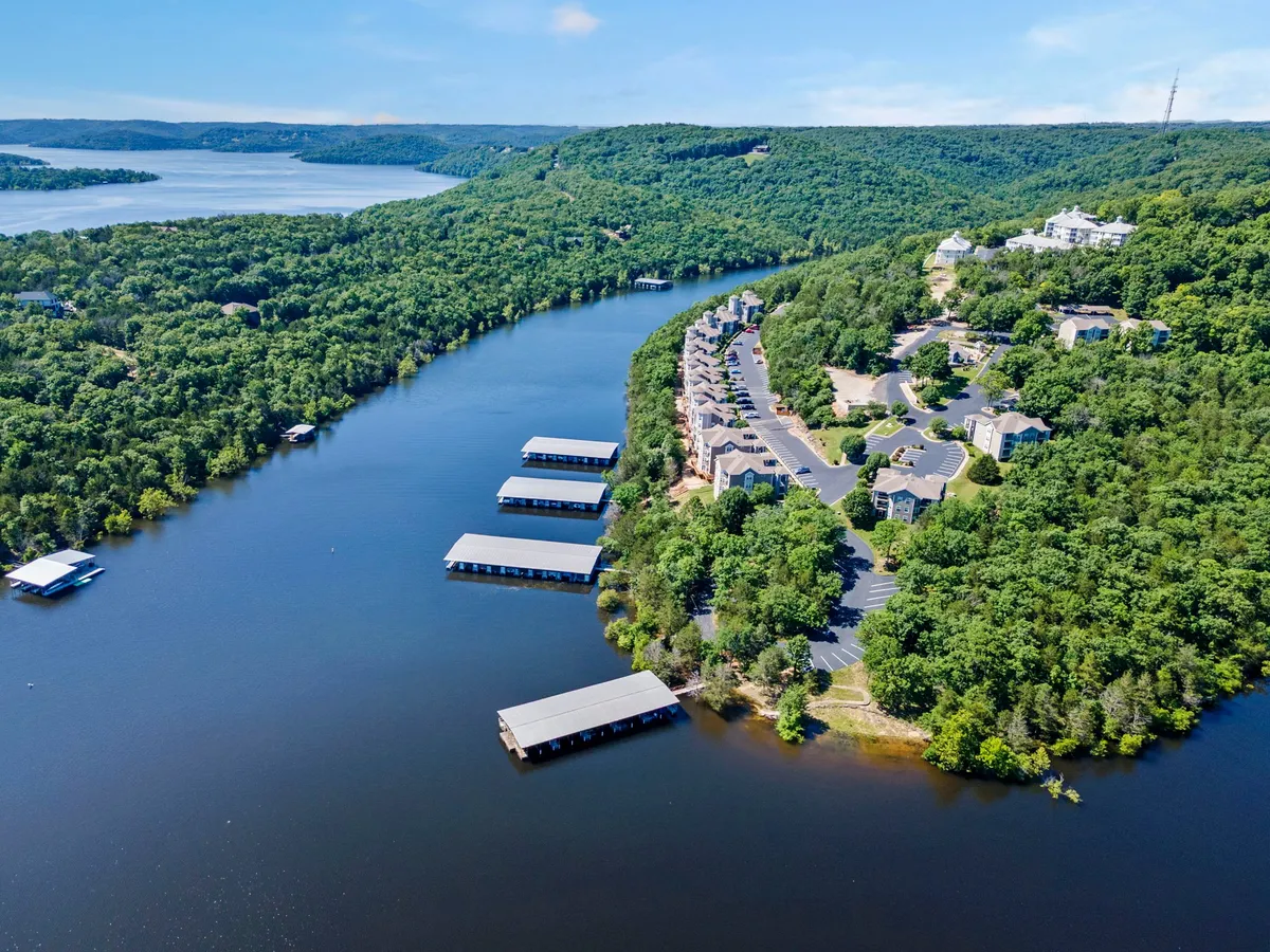 A tranquil view over a winding river bordered by lush green landscape, with boathouses and residential buildings in the background. The scene exudes calm and offers a glimpse of the kind of lakeside exploration and breathtaking vistas couples can enjoy together.