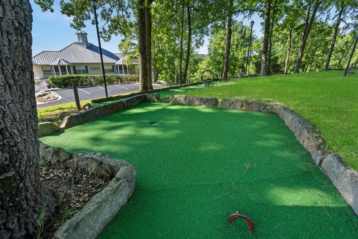 This image features a cheerful mini golf area nestled among green turf and mature trees, bordered by stone accents. Outdoor seating and the surrounding natural landscape evoke a playful, family-friendly ambiance perfect for shared recreation.