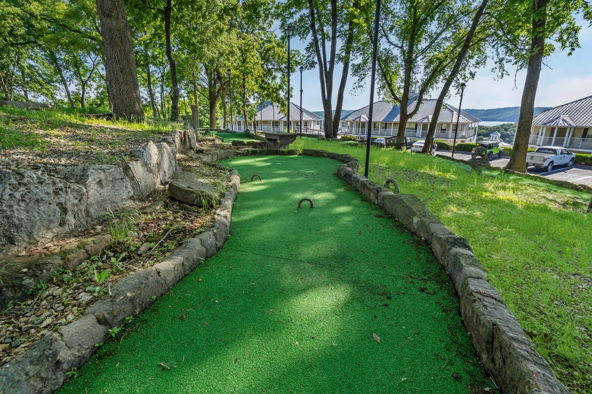 A vibrant shot of the mini-golf course surrounded by lush greenery and stone pathways. People can imagine playful competition and group gatherings in this inviting outdoor leisure area.