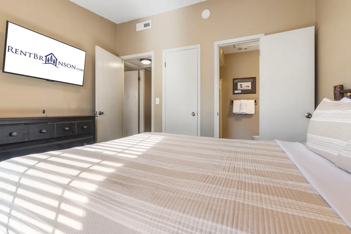 A welcoming bedroom with a bed dressed in striped bedding, a wall-mounted television, and an open door leading to an ensuite bathroom. The room’s relaxed décor and easy bathroom access echo the emphasis on privacy and convenience.