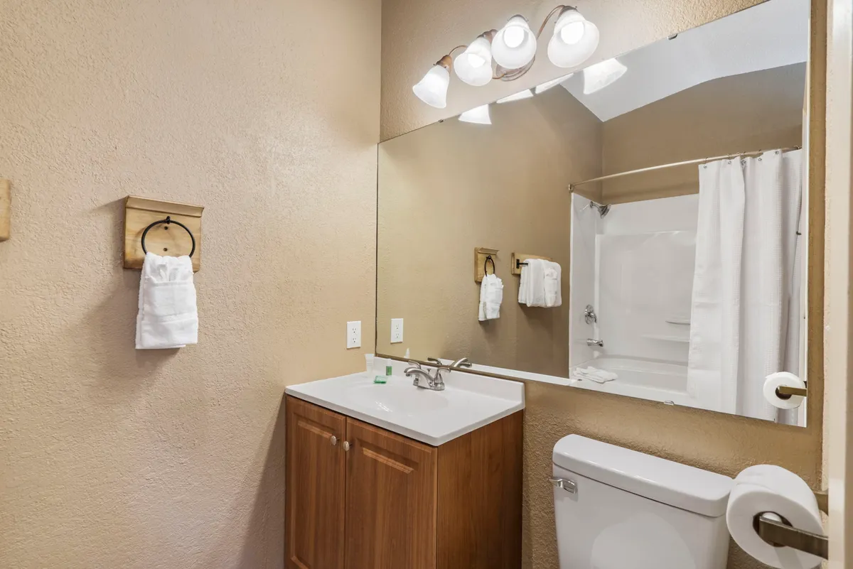 A clean, modern ensuite bathroom featuring a sleek vanity sink, large mirror, fresh towels, and a glass-enclosed shower. The design is practical yet inviting, perfect for unwinding with a refreshing shower or self-care routines.