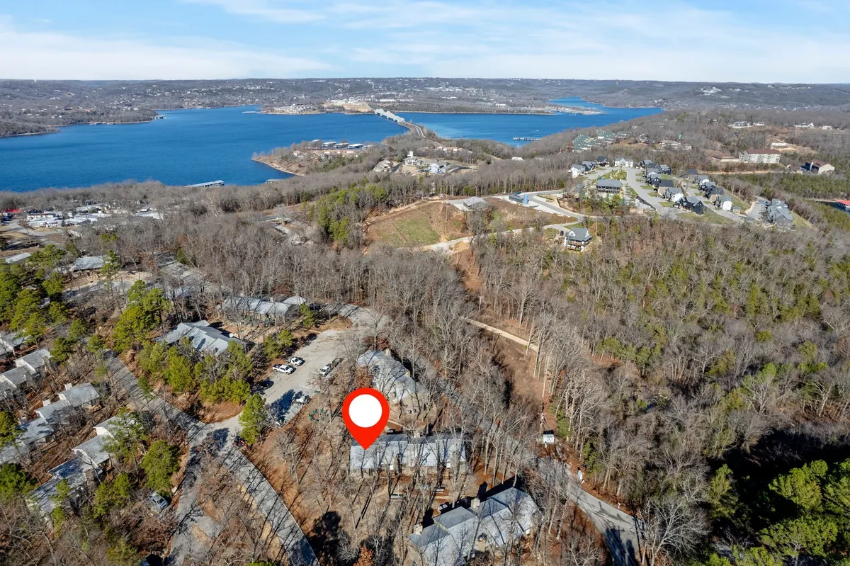 A tranquil lake surrounded by wooded areas and nearby residential buildings, with trails seemingly leading toward the water. The soft lighting evokes a sense of calm and connection to nature.